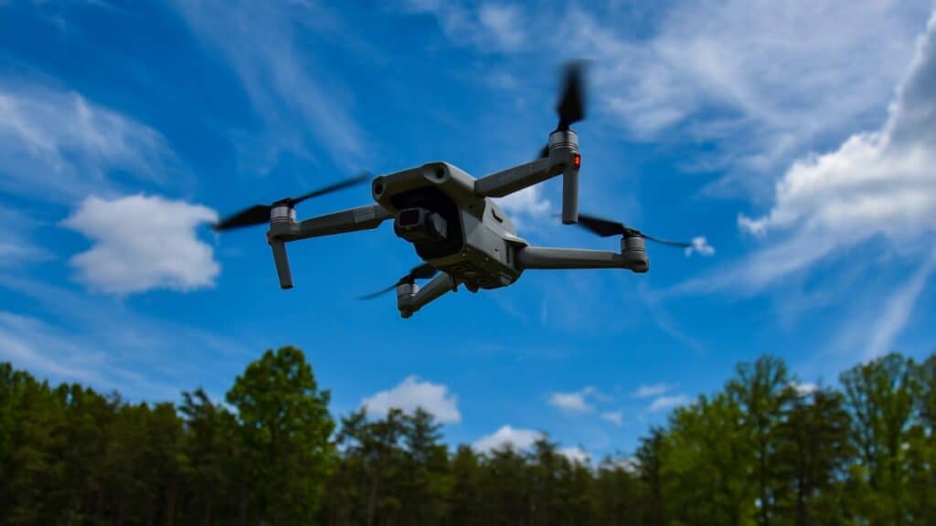 Drone flying next to a forest and above a grassfield.