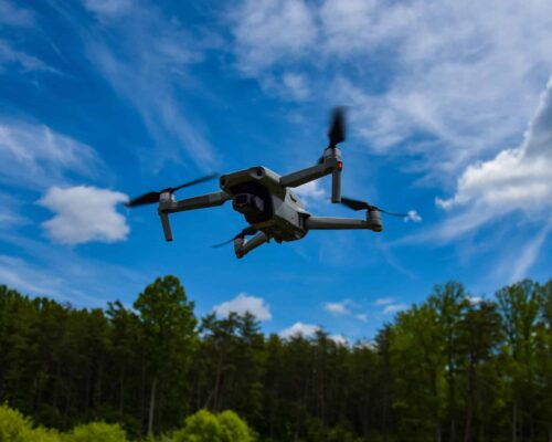 Drone flying next to a forest and above a grassfield.